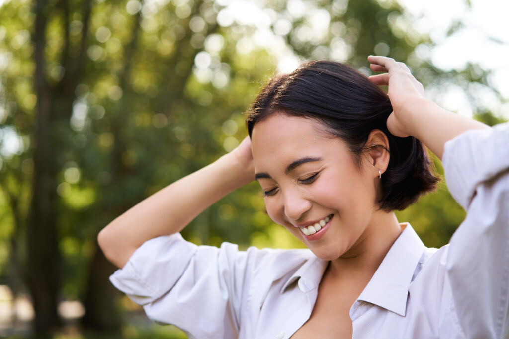 beautiful young woman tying her hair while walking in park, smiling romantic, enjoying warm day