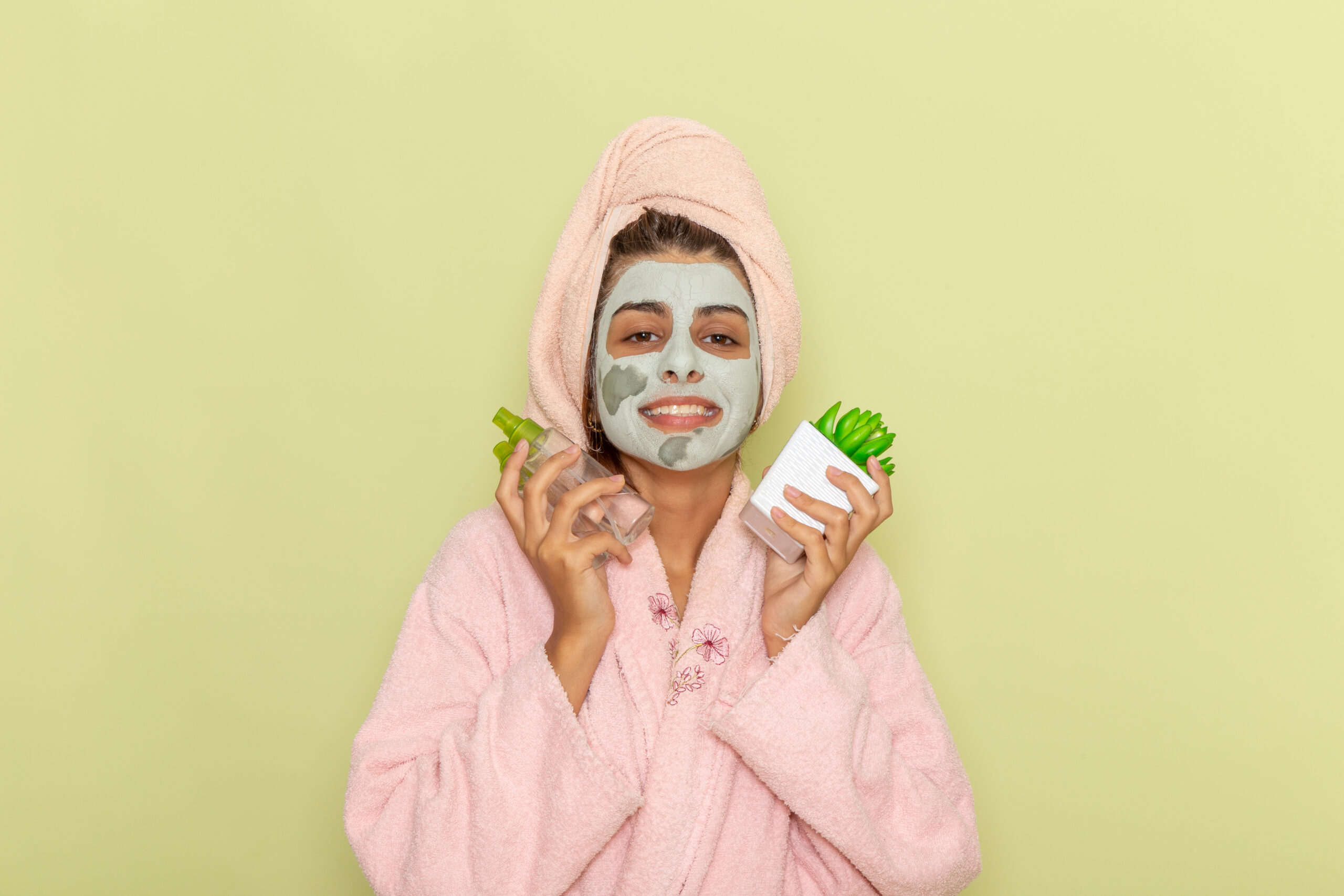 front view young female after shower pink bathrobe holding make up removers smiling green surface