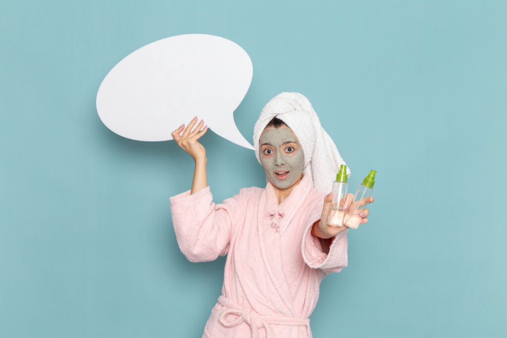 front view young female pink bathrobe holding white sign sprays blue wall beauty water bath cream selfcare shower