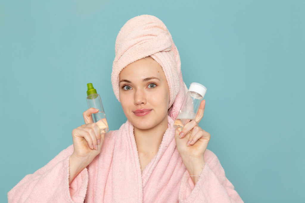 young female pink bathrobe holding make up flasks blue